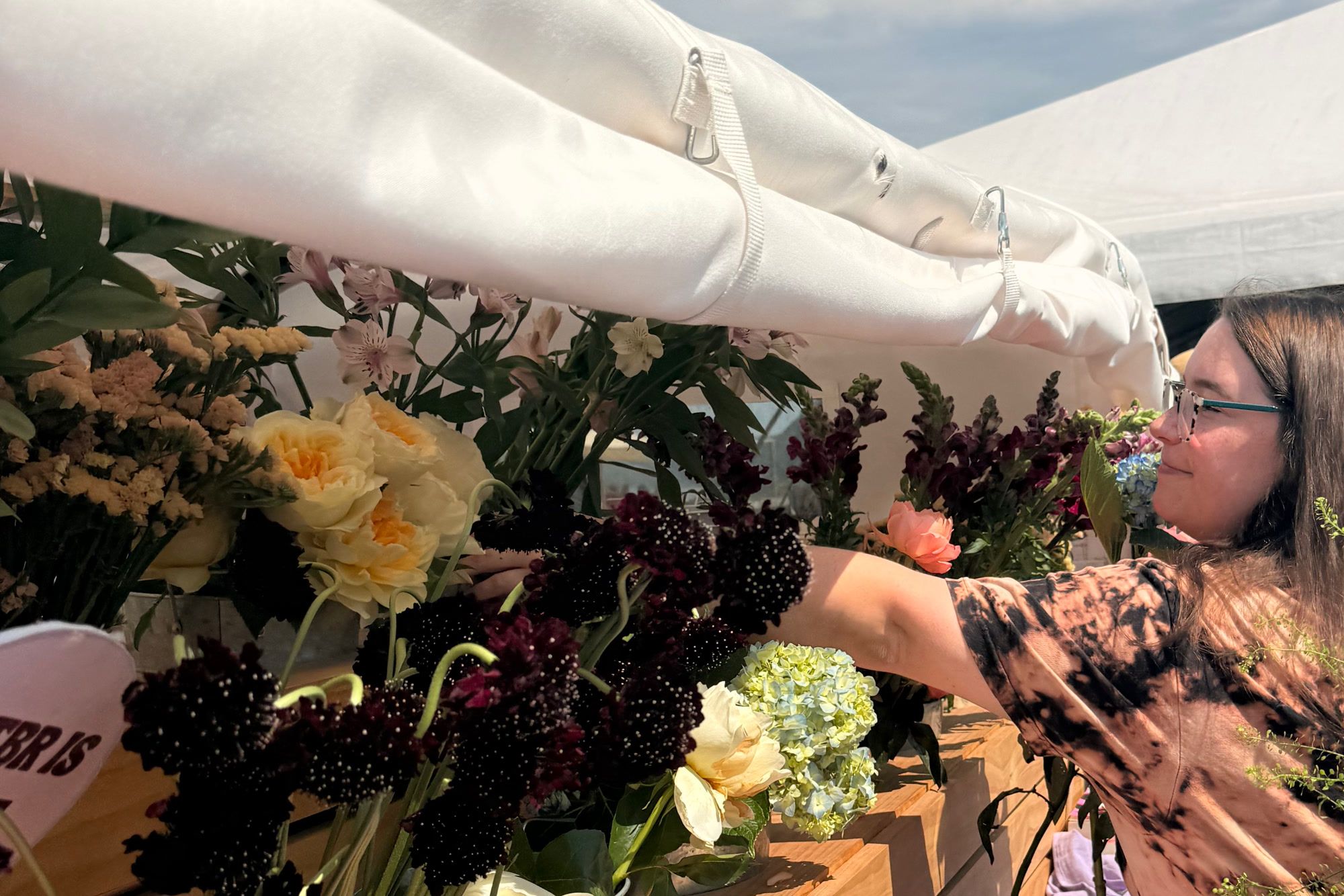 A guest reaching into buckets of fresh dahlias, roses and greenery arranged along Rosi's wooden truck bed under her white canopy.