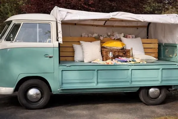 Side view of Rosi, a teal 1962 Volkswagen single-cab pickup, with a canvas canopy over her bed and a picnic setup of cushions and a wicker basket inside.