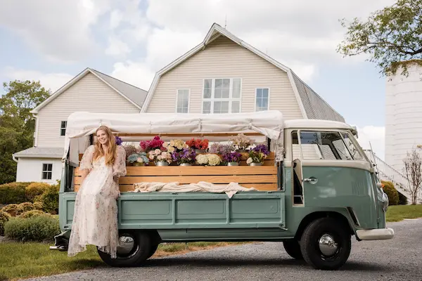 Rosi, a vintage mint green VW event truck, styled with colorful flowers beside a woman in a floral dress at a countryside venue.